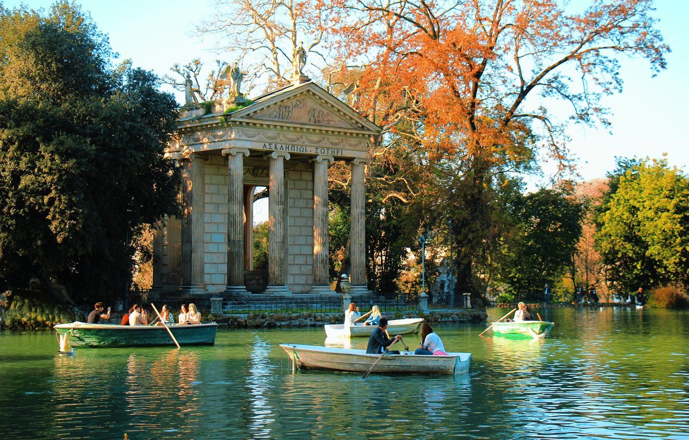 Rowing boats on a lake in front of a small classical temple, in autumn colours
