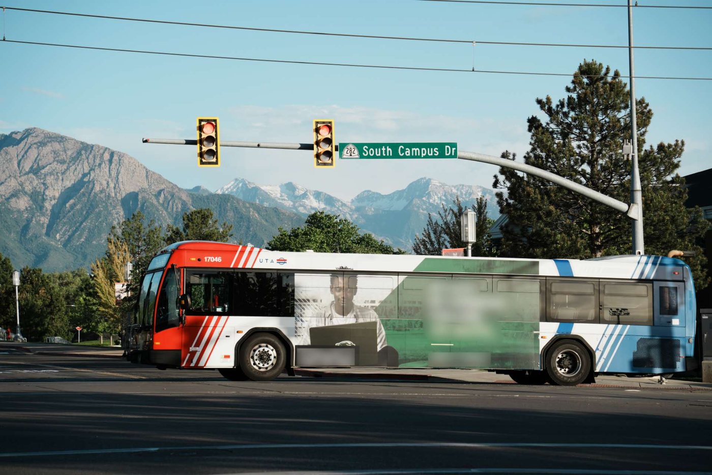 A UTA bus passing under the South Campus Drive sign, snow-capped mountains behind