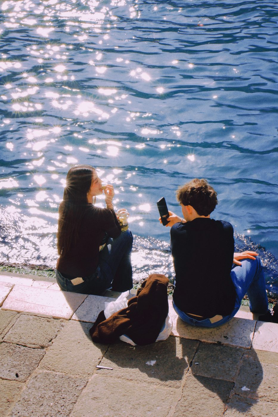 Two people sitting at the water's edge, the lagoon glittering in the sun