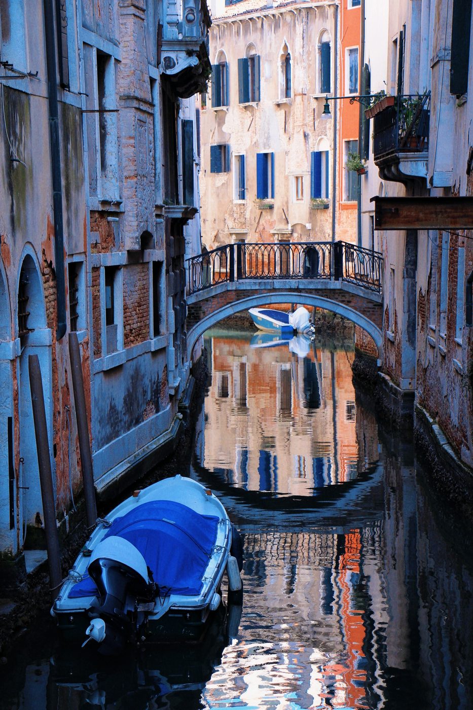 A small bridge over a quiet side canal, a blue-covered boat in front