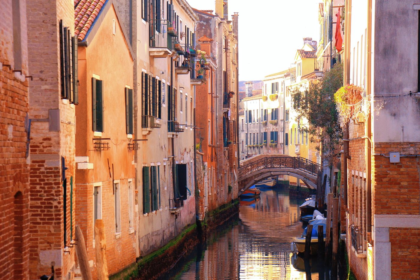 A gondolier passing under a footbridge on a narrow canal, in warm evening light